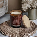 A scented candle with a wooden lid on a woven mat, with dried flowers in the background.